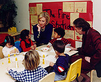 Clinton sits with children in a classroom