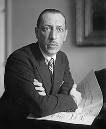 Stravinsky resting his arms atop a piano, a score under his arms