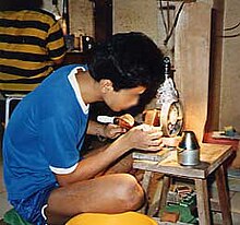 An Asian man bent over a small gemcutting machine on a low table.