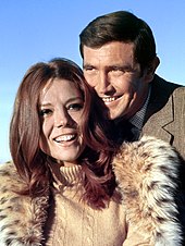 Lazenby and Rigg are shown in close up, smiling with their heads close together