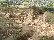 A low stone wall being excavated, with a town in the background.