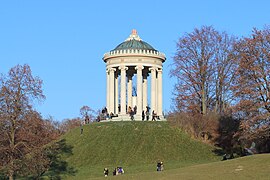 Monopteros auf künstlichem Hügel im Englischen Garten in München. 1832 wurde auf dem ursprünglich flachen Gelände ein 15 Meter hohes Fundament aus Backstein geschaffen, im Laufe mehrerer Jahre durch Erdaufschüttung überhügelt und darauf der Rundtempel errichtet.[17]