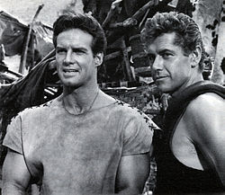 A black and white photograph of two white muscular men in vaguely ancient short-sleeve shirts.