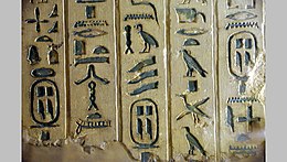 Square fragment of a light brown wall covered with inscribed hieroglyphs painted in green color