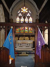 altar of a neo-Gothic church, showing colourful stained glass windows, with two flags posted in the foreground