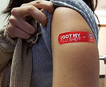 A young woman displays her bandage after receiving the vaccine at a drug store