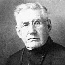 Black-and-white portrait of a white-haired man wearing glasses.