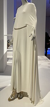 Floor-length white dress with sleeves, attached cape and gold chain belt