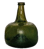 A squat semi-transparent green blown glass bottle, shaped vaguely like a squarish mandarin citrus, with a strongly concave base and a short flanged neck.