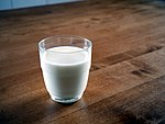 A clear glass of white milk on a brown wood table against a dark backdrop