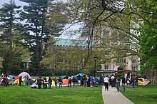 tents, signs, and people standing on green grass in front of the Vassar College Library