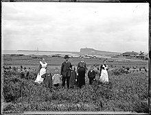 Mrs. and Mr. A. Graham's family standing at Stockton with breakwater, masts of shipwreck, and Nobby's Head in background.