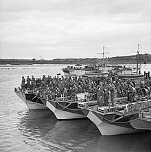 Photograph of a large group of soldiers standing on board landing ships