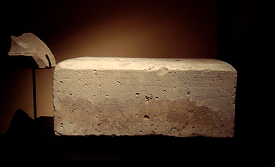 A large white cuboid block, with engraved Greek script visible along one side.