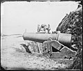 The foreground weapon is a 10-inch Model 1844 columbiad, banded and rifled, recently captured by the Union at Fort Johnson in Charleston Harbor. The carriage has been cut through by the Confederates to deny the weapon's use to the Union.
