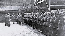Charles Edward shaking hands with one of a line of soldiers wearing German military uniforms