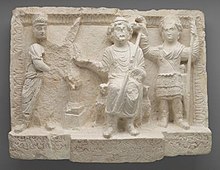 Limestone relief sculpture with three figures, the one on the right (in military dress) holding a crown over the head of the figure in the middle.