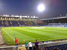 Fratton Park football stadium at night, home of Portsmouth F.C. The pitch is lit by floodlights.