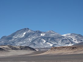Photo: A broad, irregular mountain in an unvegetated landscape with sparse snowpatches