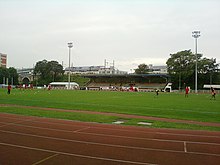 Players in red and white on a football pitch, with a running track in the foreground of the picture.