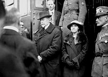 A serious-looking Masaryk and his daughter getting off a train, surrounded by people