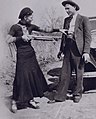 Bonnie with a shotgun reaches for officer Persell's pistol in Clyde's waistband.[3]