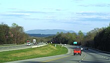 Driver's view of a six-lane divided highway with mountain peaks in the background