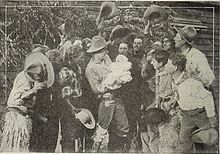 A crowd looks on as a man holds up a newborn