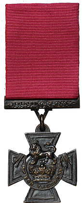 A bronze Cross pattée suspended from a crimson ribbon