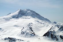 A snow-covered, cone-shaped mountain overlooking snow-covered and exposed slopes.