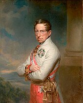 Half-length oil portrait of the Archduke Charles by Georg Decker. Charles wears a white high-collared military jacket of the Austrian army and has a red and white sash over his right shoulder. He wears two decorations, a cross on his breast and another medal at his neck. He has a long fleshy face, short brown hair, and light eyes, and gazes calmly towards the viewer. His arms are folded across his chest.