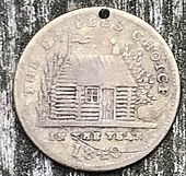 A worn, holed brass token with a log cabin and cider keg on it, and reading "the people's choice in the year 1840"