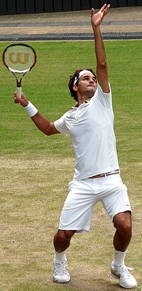 A tennis player in the middle of his service motion, arms and eyes raised