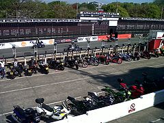 View from the Grandstand seating area showing pit-boxes with refuelling stands, then-used for visitor bike-parking on a non-race day, with scoreboard to far side across the Glencrutchery Road