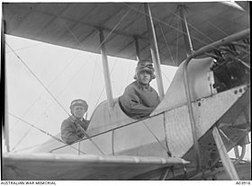 Two men in flying gear seated in tandem open cockpits of a biplane