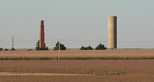 Tall brick chimney and cylindrical concrete water-tower standing alone in cornfield