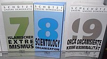 Display with three types of information leaflets, with the numbers and titles "7 Islamischer Extremismus" (coloured in shades of green), "8 Scientology Organisation" (coloured in shades of blue) and "9 Organisierte Kriminalität" (shades of grey). At the top of each leaflet is the inscription "Schützt unsere Demokratie".
