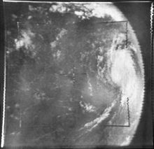 Grayscale image of a tropical cyclone as viewed from space. Due to the position of the camera, the tropical cyclone is at center-right, with banding features visible. As a result of the camera angle, the limb of the Earth is clearly visible; outer space appears a uniform dark gray.