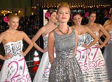 Heigl in a grey and silver dress, behind her several women wearing the same white dress from the film poster