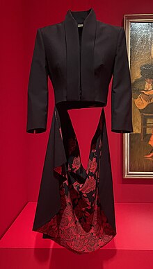 Black jacket, cut short in front with a long tail, which is lined with patterned red and black fabric