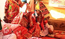 A festively-dressed couple sits cross-legged on the floor