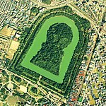 Bird eye view of a large keyhole-shaped island surrounded by a moat and trees.