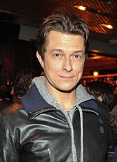 A man in a leather jacket smiling at the camera