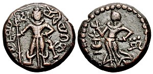 Yaudheya coin, imitative of Kushan coinage, 3rd-4th centuries CE. Obverse: Karttikeya standing facing, holding a spear with dvi (“two” in Brahmi) to the left of Karttikeya's head, peacock to lower right, Brahmi legend around: 𑀬𑁅𑀥𑁂𑀬 𑀕𑀦𑀲𑁆𑀬 𑀚𑀬 (yaudheya ganasya jaya, “Victory to the Yaudheya people”). Reverse: Devasena standing left, raising hand; flower vase to left, inverted nandipada to the right.[1] of