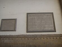 Two plaques on a white wall from a low point of view.