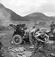 Soldiers firing a howitzer against a mountainous backdrop