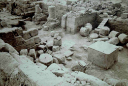 Low ruins of a temple with rubble, a large cubic block of granite at their centre.