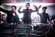 Three men stand behind DJ decks