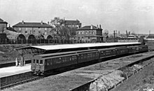 A black-and-white photograph showing a 6-car train at a station. There are detail differences in the carriages, the leading car, unlike the others, has its clerestory extended to the car end and the 3rd and 5th carriage sides are flared at the bottom.