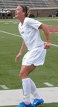 Wambach wearing a white uniform by a soccer field.